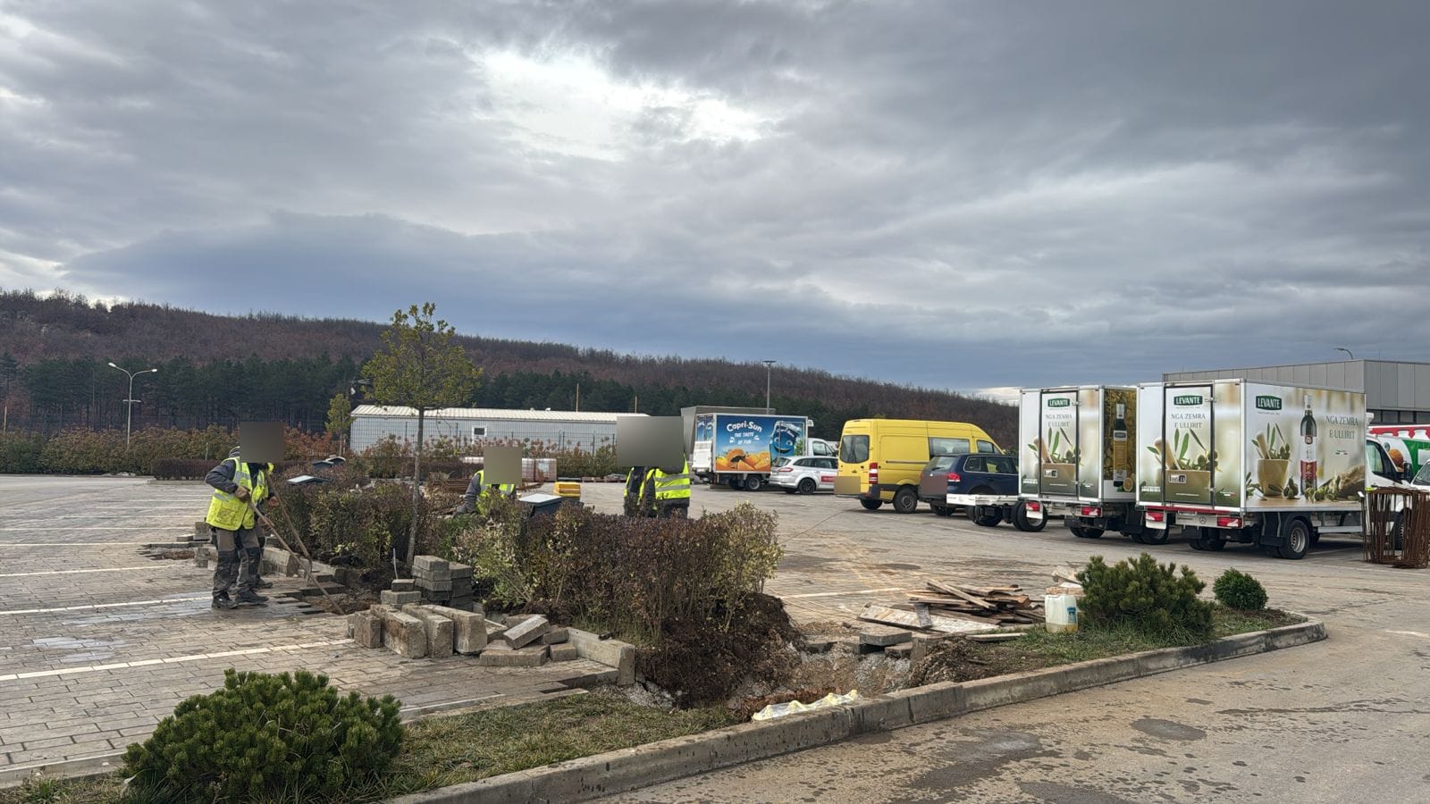 Arbeiter in Warnwesten heben am Rand eines Grünstreifens auf dem Parkplatz die Gruben für die Fundamente aus
