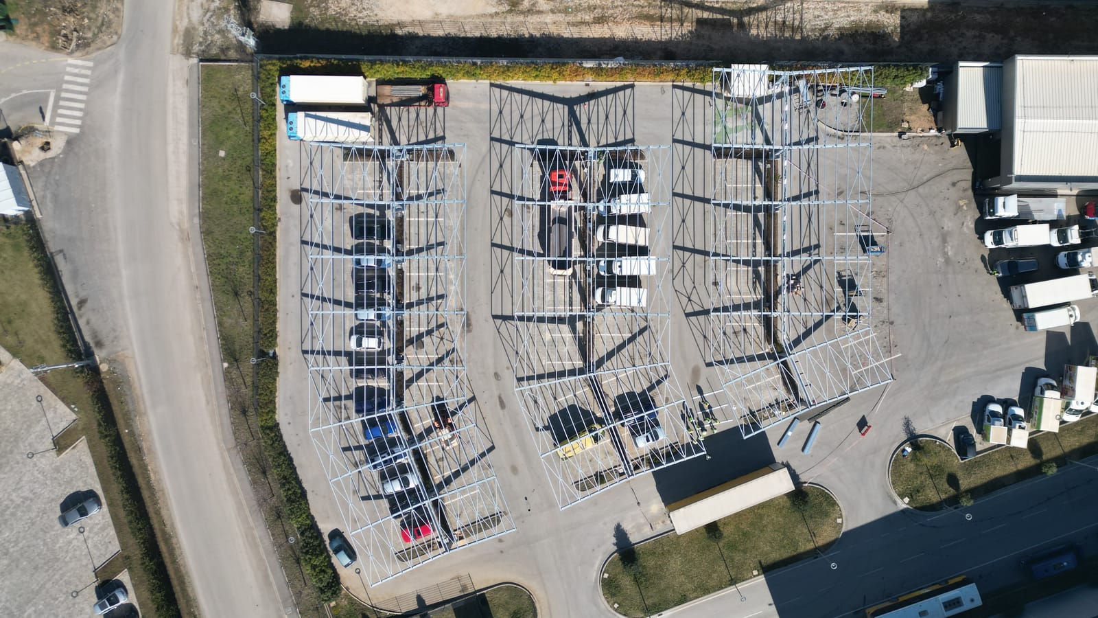 Luftaufnahme senkrecht von oben: drei Reihen Stahlrahmen über dem Parkplatz, darunter geparkte Fahrzeuge