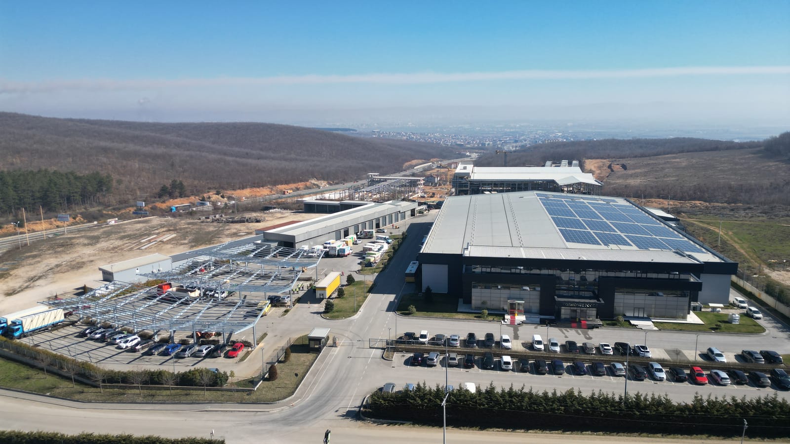 Luftaufnahme des Kosmonte-Geländes mit dem Truckport im Bau, der Produktionshalle und der Verkehrsachse im Tal