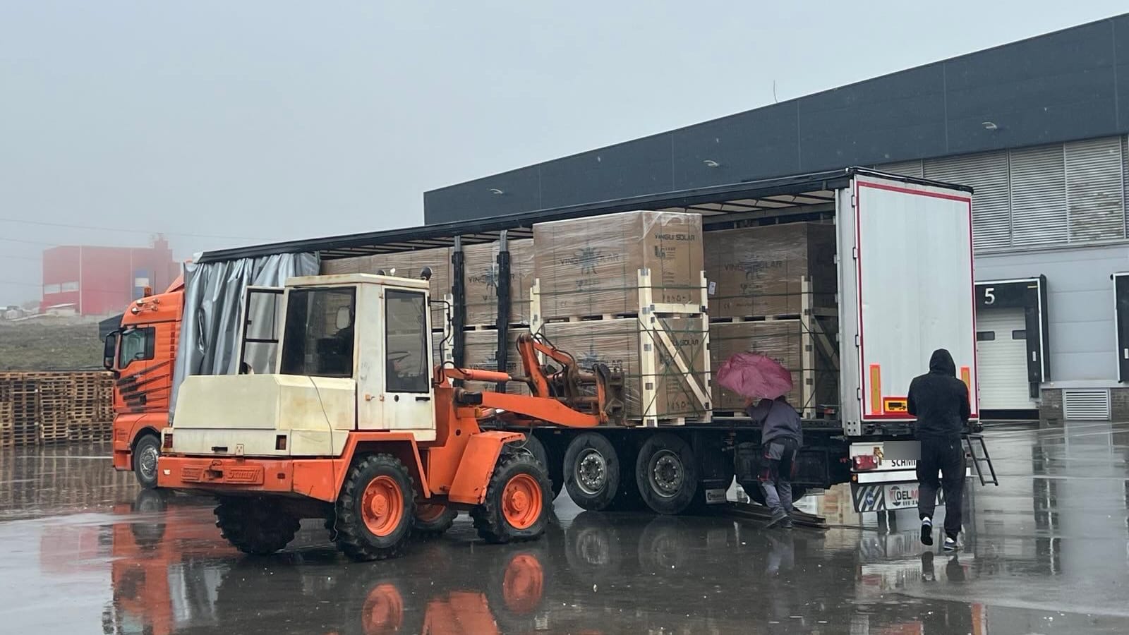 Sattelauflieger mit verpackten Solarmodulen auf Paletten, davor ein Radlader, an der Laderampe des Logistikgebäudes von Kosmonte Foods