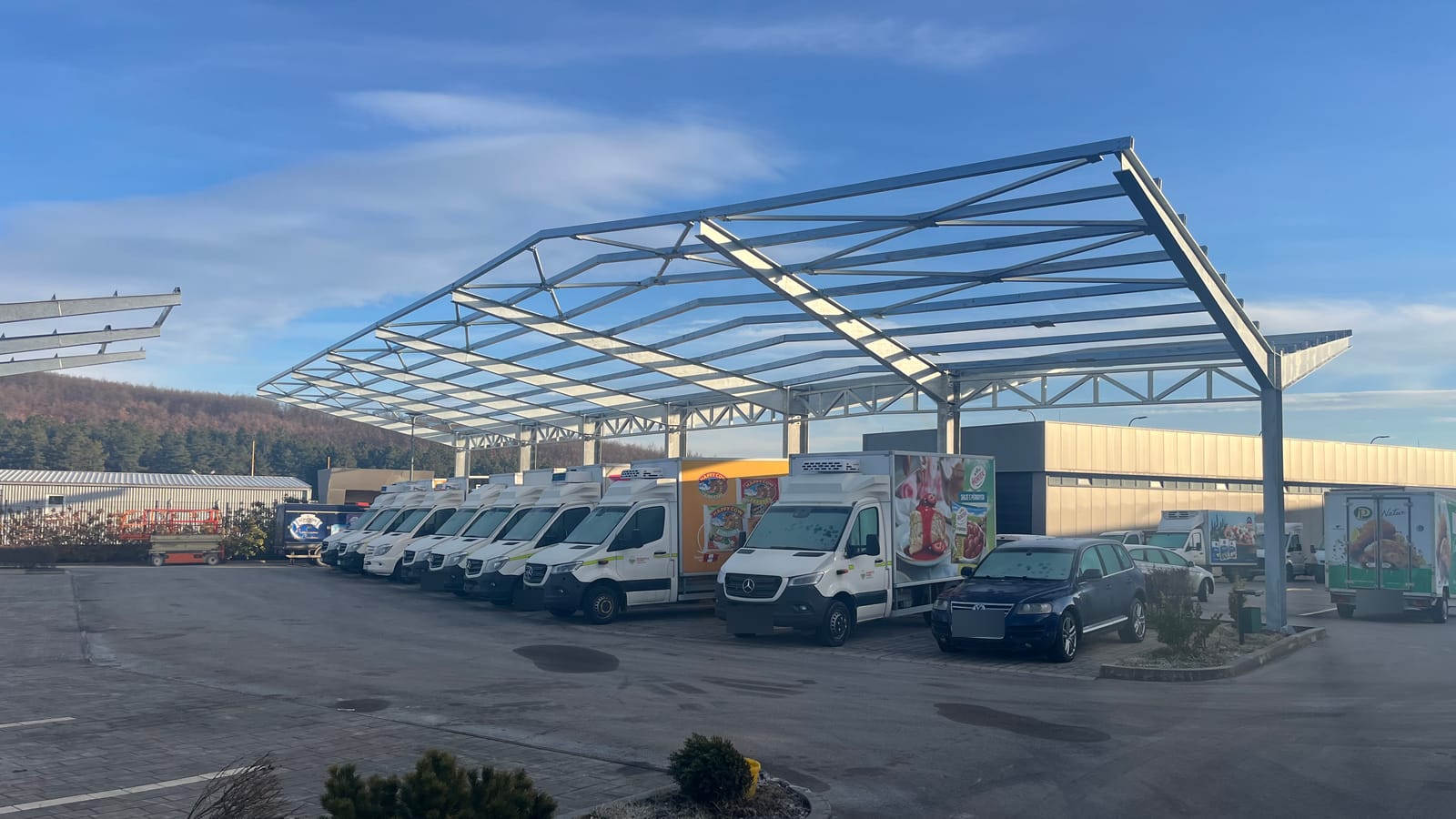 Stahlkonstruktion eines Truckport-Dachs über einer Reihe geparkter Kühltransporter