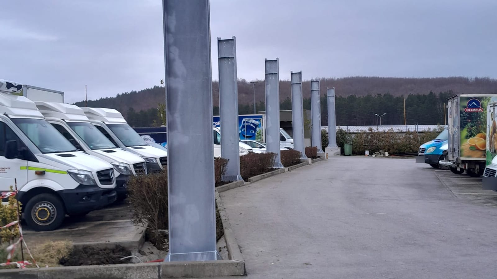 Reihe von Stahlstützen entlang einer Fahrgasse, links geparkte Lieferwagen von Kosmonte Foods
